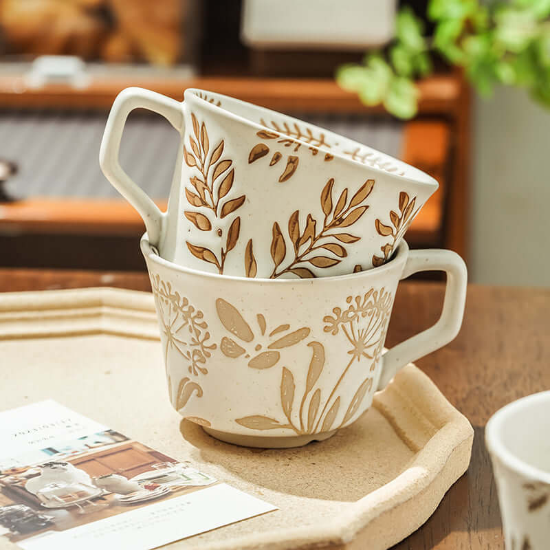 Stacked hand-painted minimalist Nordic ceramic mugs with floral designs on a wooden table.