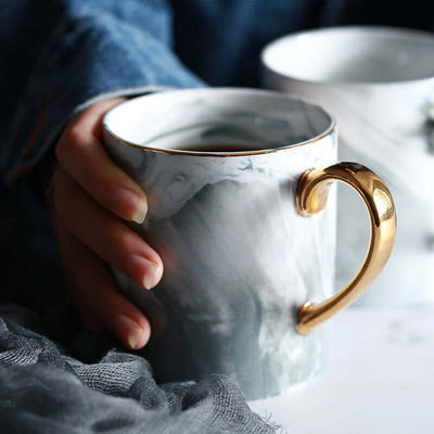 Hand holding a stylish marble ceramic coffee mug with a gold handle, perfect for 301-400ml beverages.