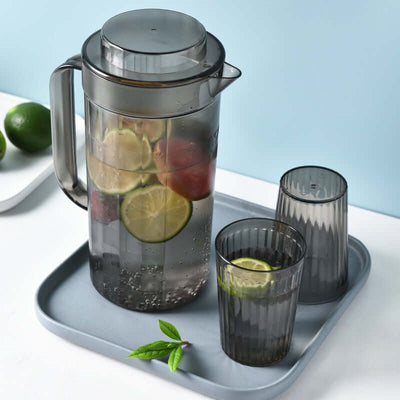Black plastic cold water bottle set with two cups on a tray, featuring fresh slices of lime inside.