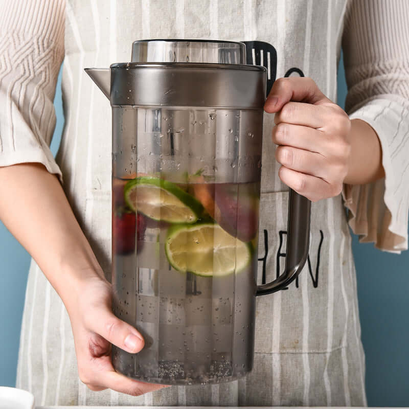 Person holding a modern black plastic cold water pitcher filled with sliced fruits, perfect for refreshing beverages.