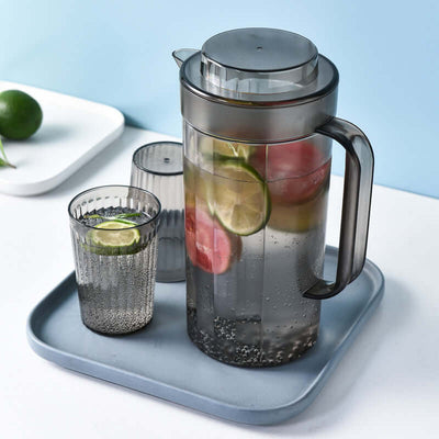Modern black plastic cold water bottle and cups set with fruit slices on a tray, perfect for refreshing drinks.