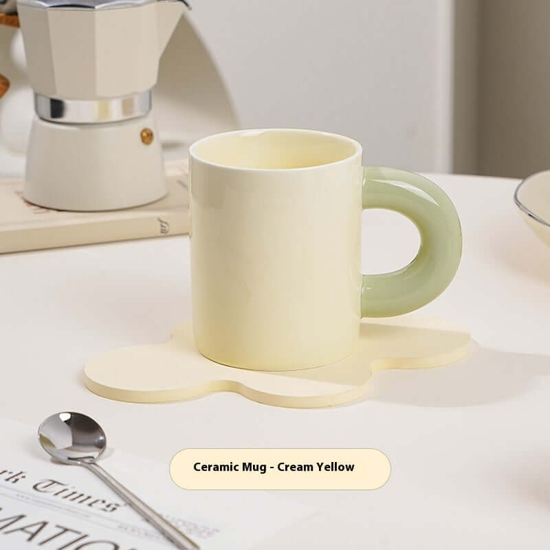 Cream yellow ceramic mug with green handle on a flower-shaped coaster, perfect for stylish drinkware.