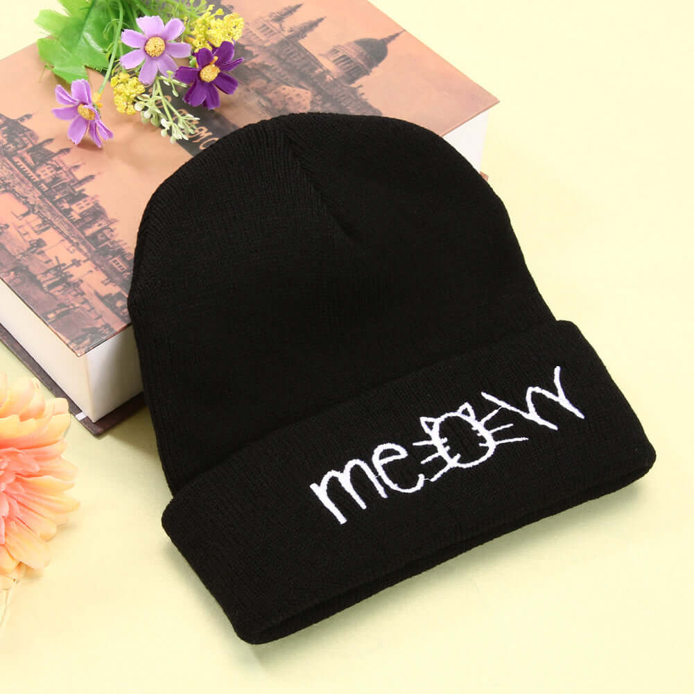 Black knitted beanie hat with 'meowy' embroidered design, perfect for casual winter wear.