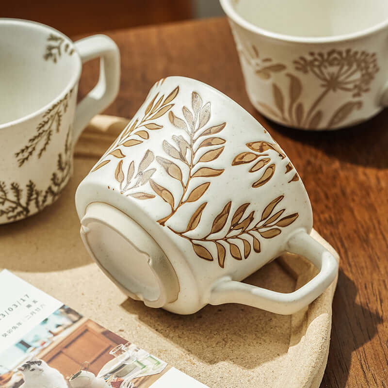 Minimalist Nordic ceramic mug with hand-painted leaf design, showcasing modern simplicity in white porcelain.