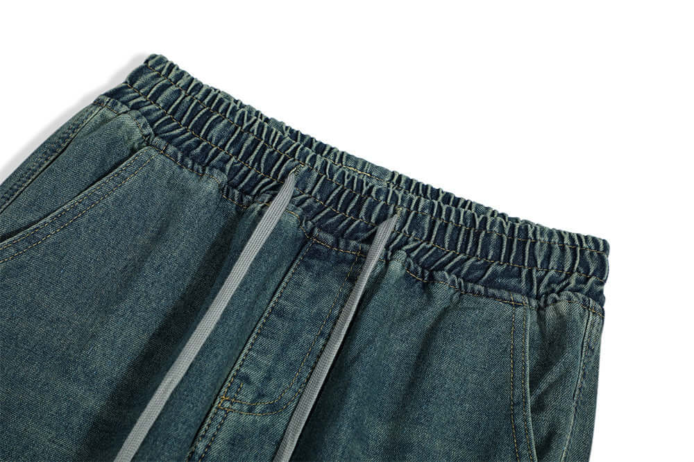 Close-up of denim trousers waistband for men, featuring elastic band and drawstrings in blue fabric.
