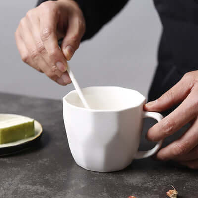 Person stirring a diamond-shaped ceramic mug on a table, perfect for retro office use.