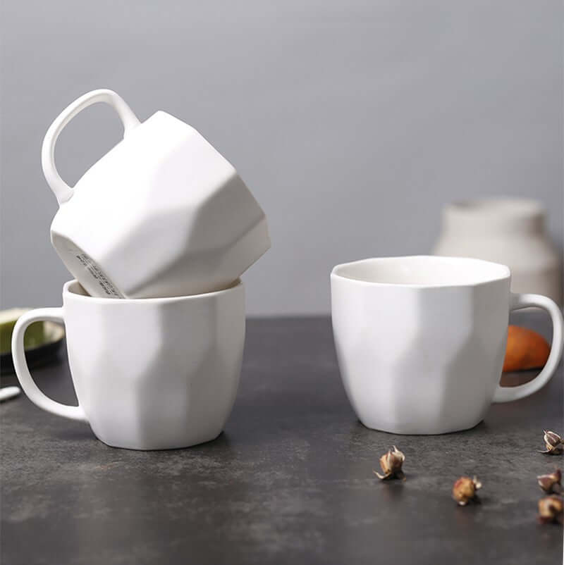 Ceramic diamond-shaped mugs in white, modern design for retro office use, styled on a dark tabletop.