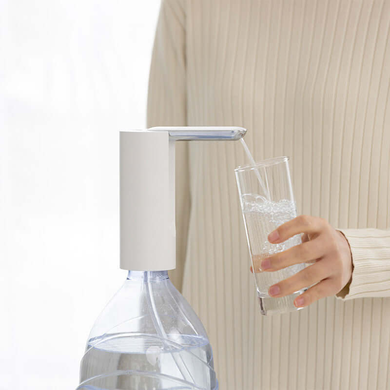 Electric household mineral water dispenser pumping water into a glass with a white water outlet pump