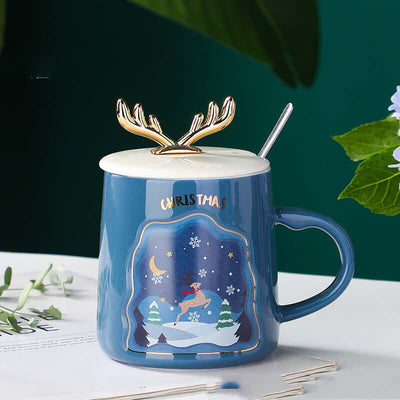 Blue ceramic Christmas mug with reindeer lid and spoon, featuring a festive winter scene and the word 'Christmas'.