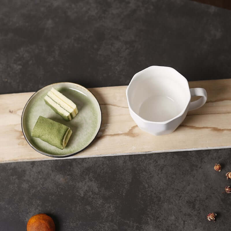 Diamond shaped ceramic mug beside a plate of green and yellow snacks on a wooden surface.
